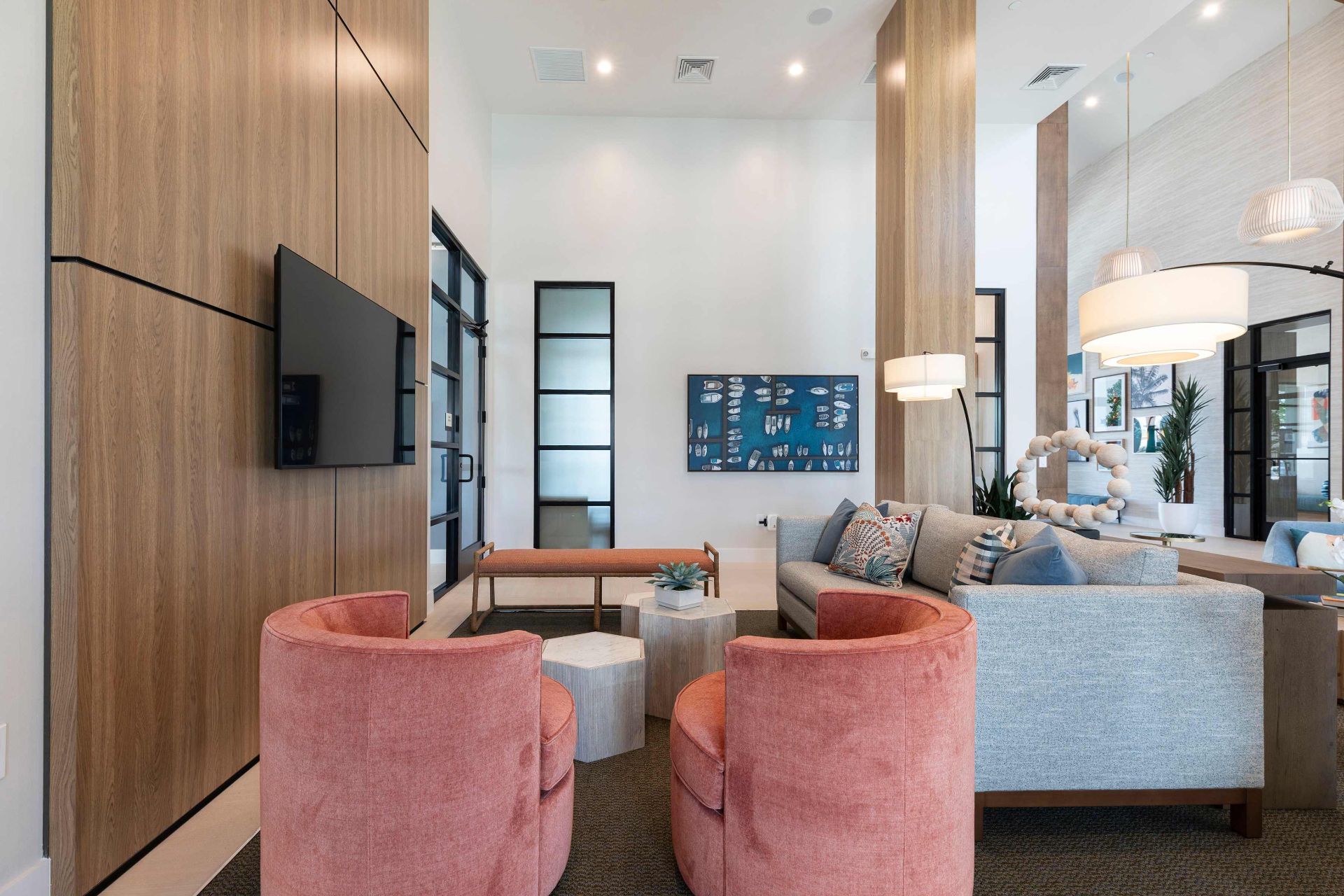 Modern living room with two pink chairs, a gray sofa, a mounted TV, and wooden accent walls. Contemporary decor and pendant lights are visible.