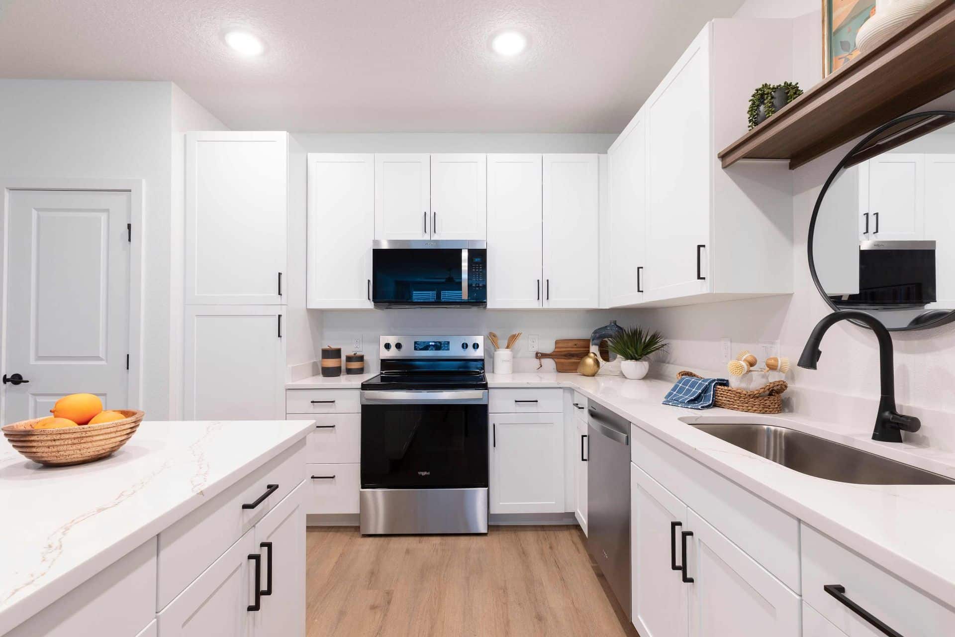 Modern kitchen with white cabinets, stainless steel appliances, a black faucet, a bowl of oranges on the counter, and wooden flooring.
